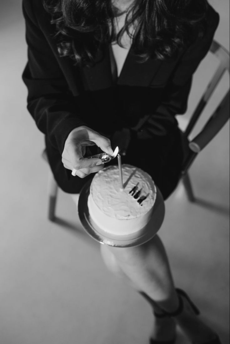 a woman sitting in a chair cutting into a cake with a pair of scissors on it