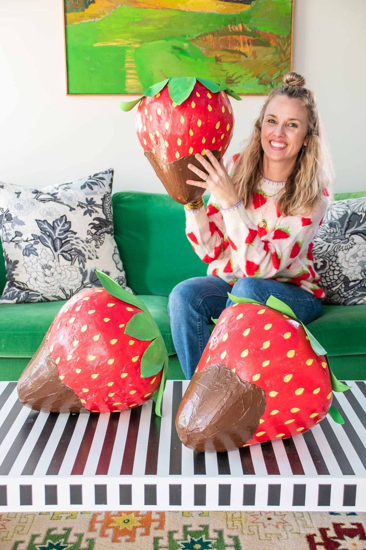 a woman sitting on top of a green couch holding two giant strawberries