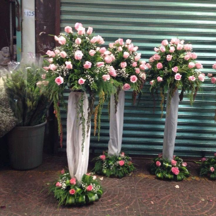 three tall vases with pink roses and greenery on the side of a building