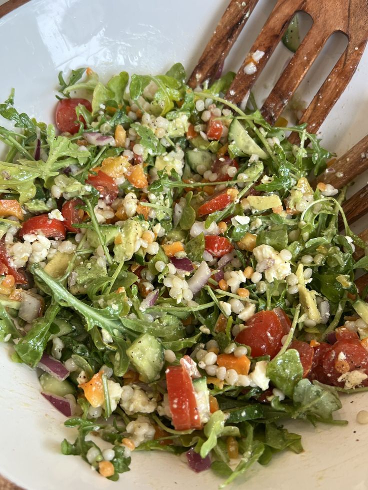 a salad in a white bowl with wooden utensils