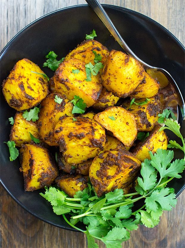 a black bowl filled with potatoes and cilantro on top of a wooden table