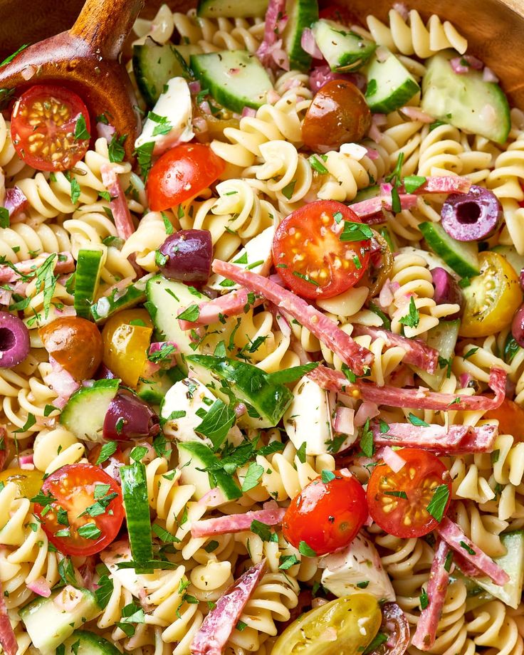 pasta salad with tomatoes, cucumbers, olives and onions in a wooden bowl