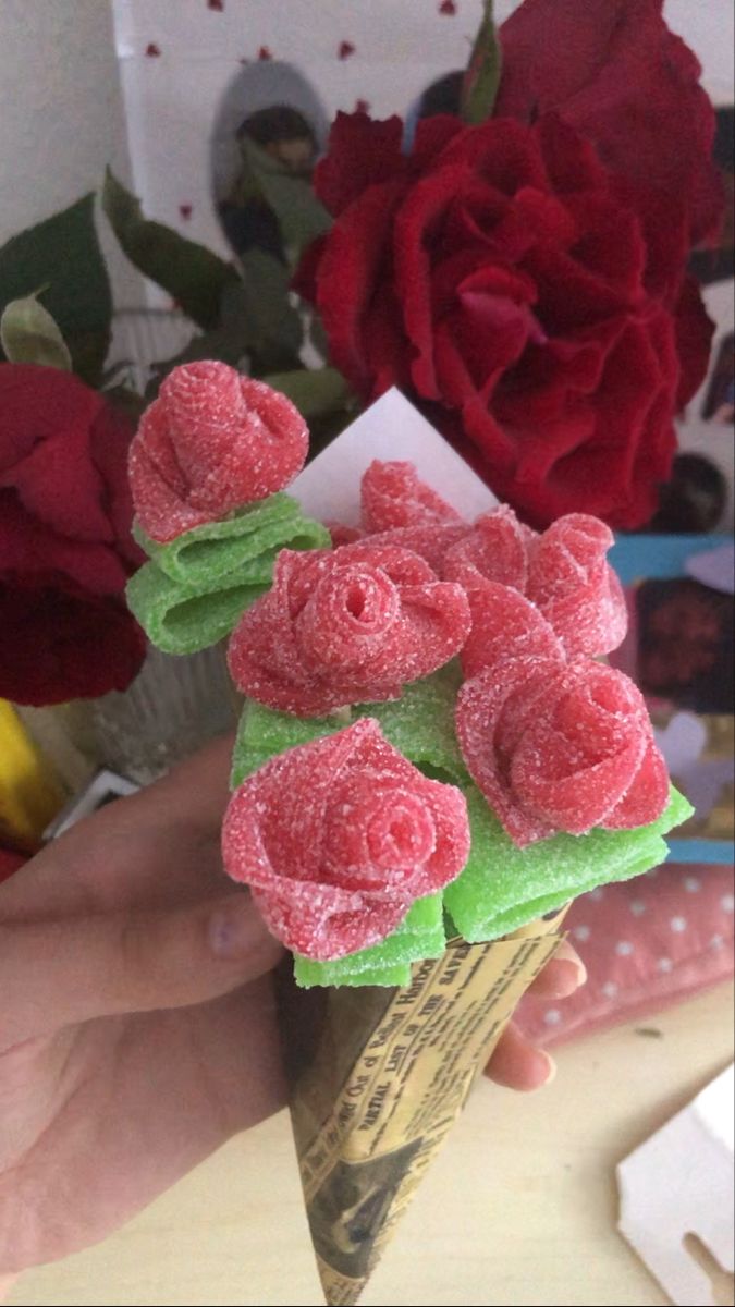 someone is holding an ice cream cone with flowers on it in front of some roses