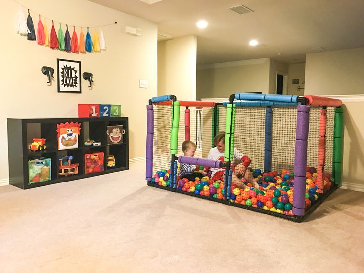 two children playing in a playpen with balls on the floor and toys behind it