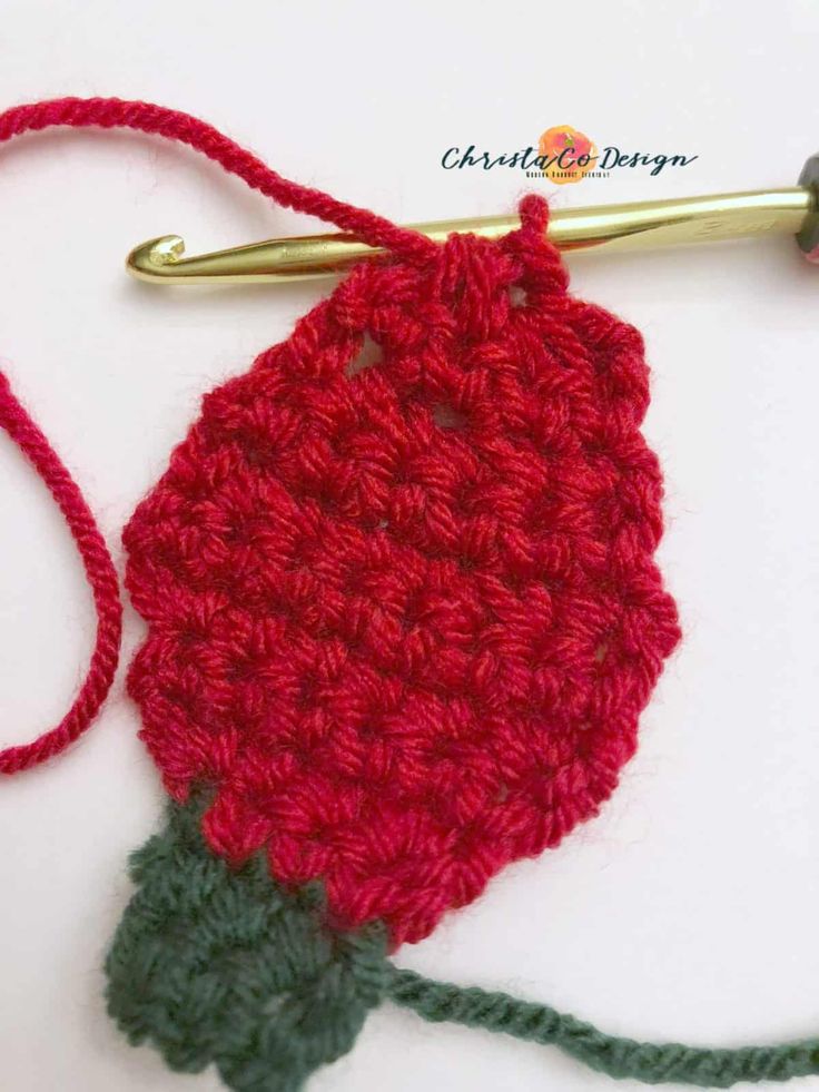 a crocheted red flower with green leaves on it next to a knitting hook