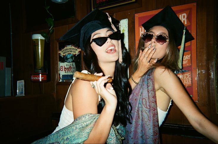 two women in graduation caps and gowns pose for the camera while one eats a donut