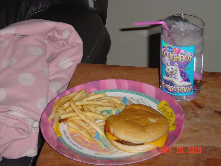 a hamburger and french fries on a pink paper plate next to a bottle of water