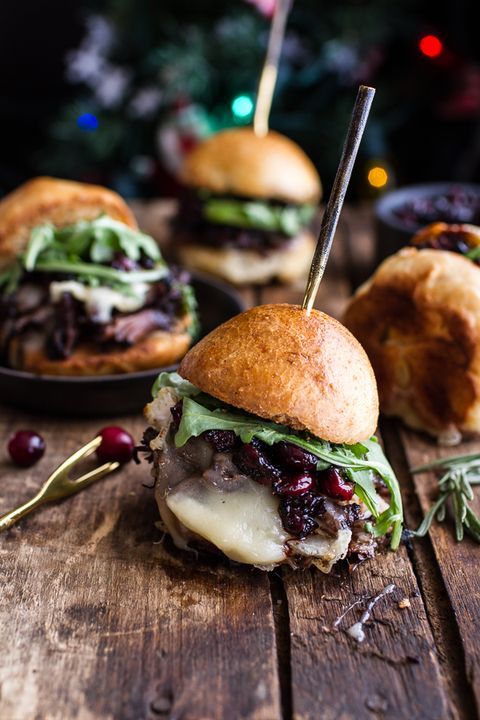 two sandwiches with meat, cheese and cranberry sauce on a wooden table next to a christmas tree