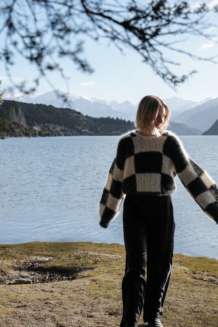 a woman standing on top of a grass covered field next to a lake