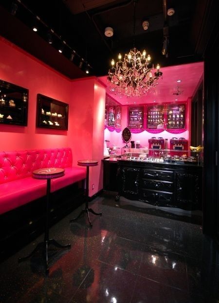 a pink room with black furniture and chandelier hanging from the ceiling in front of a bar