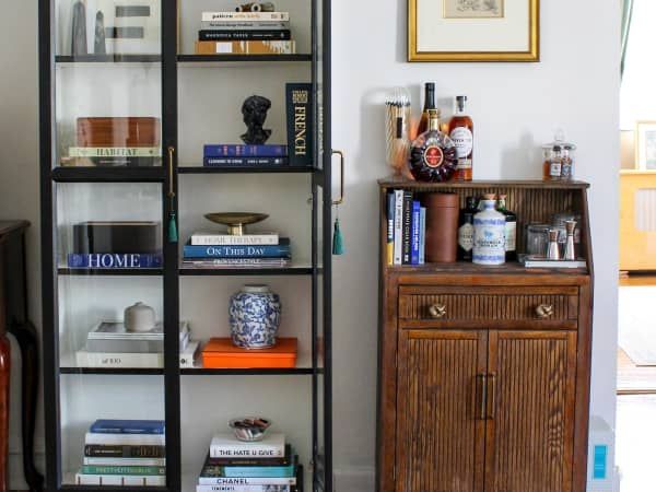 a book shelf with many books on it in a living room next to a dresser