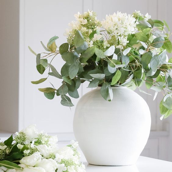 a white vase filled with flowers sitting on top of a table next to a green plant