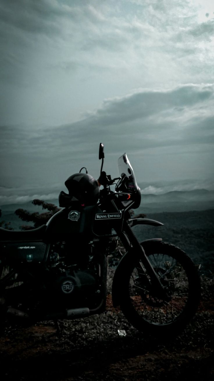 a motorcycle parked on the side of a hill under a cloudy sky with dark clouds