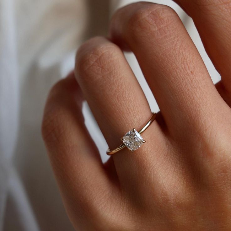 a woman's hand with a diamond ring on top of her finger, wearing a white shirt