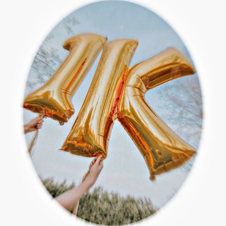 two people holding gold balloons in the shape of letters k and person's hand