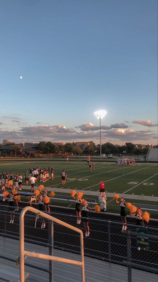 a football field with fans holding orange pom poms and watching the sun go down