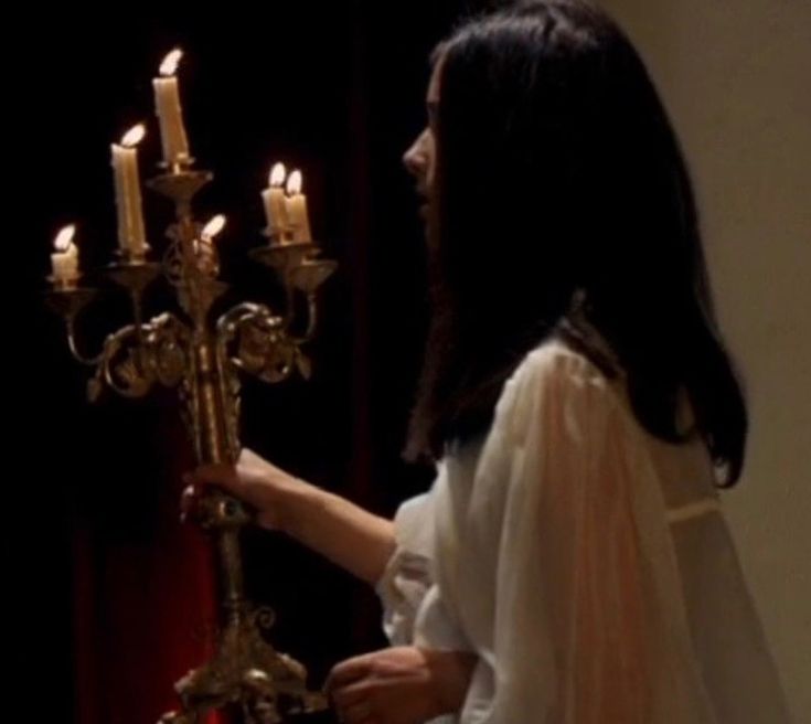 a woman in white dress holding up a candelabra with candles on it