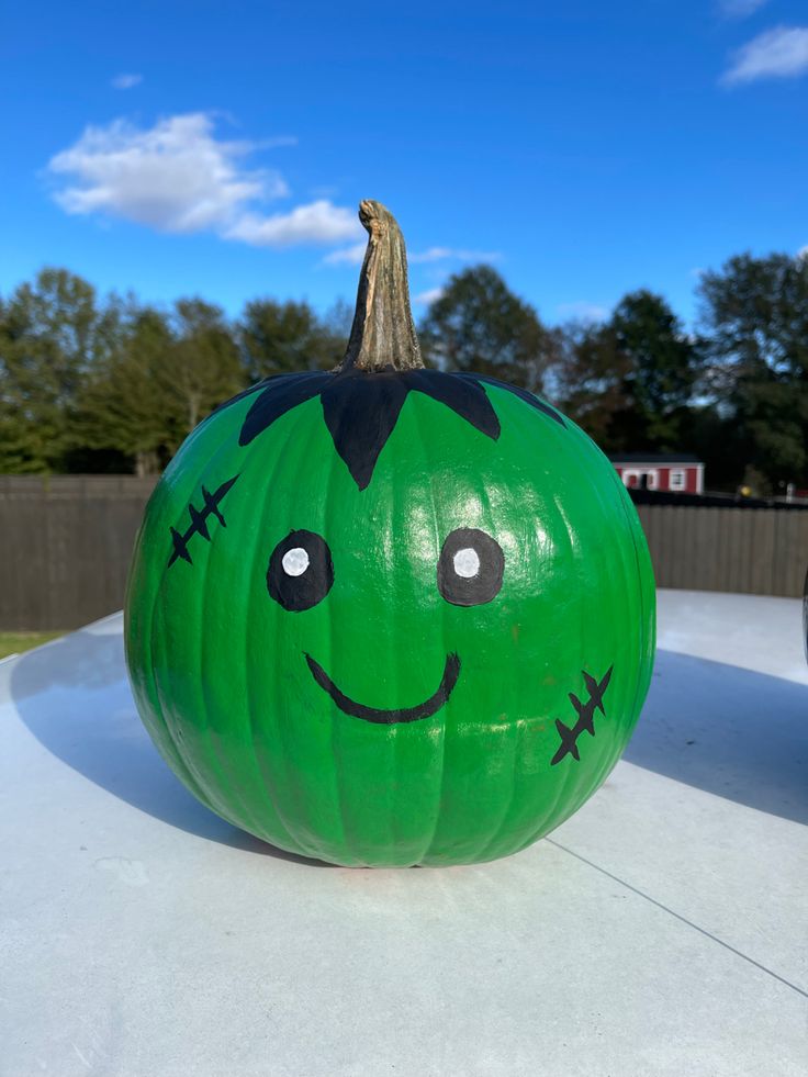 a large green pumpkin with a face drawn on it's side sitting on top of a white surface