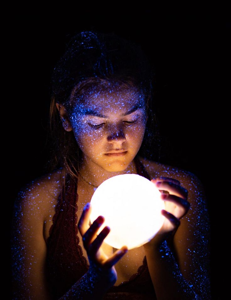 a young woman holding a glowing ball in her hands with blue light shining on her face