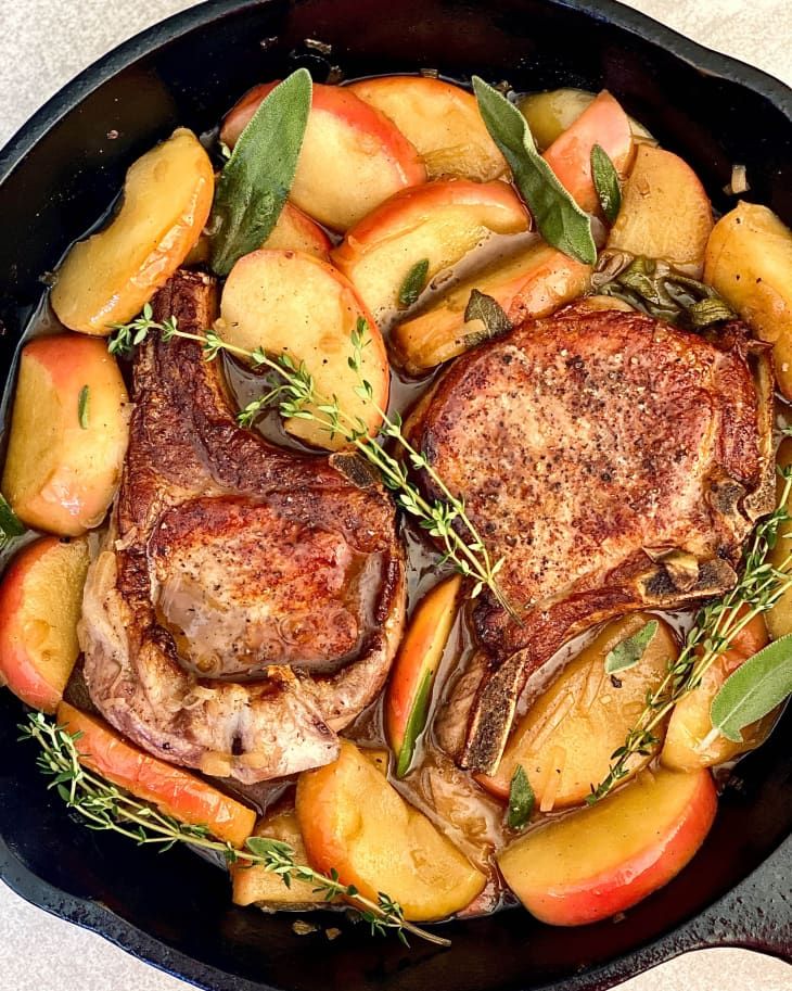 pork chops and apples in a cast iron skillet with herbs on the side