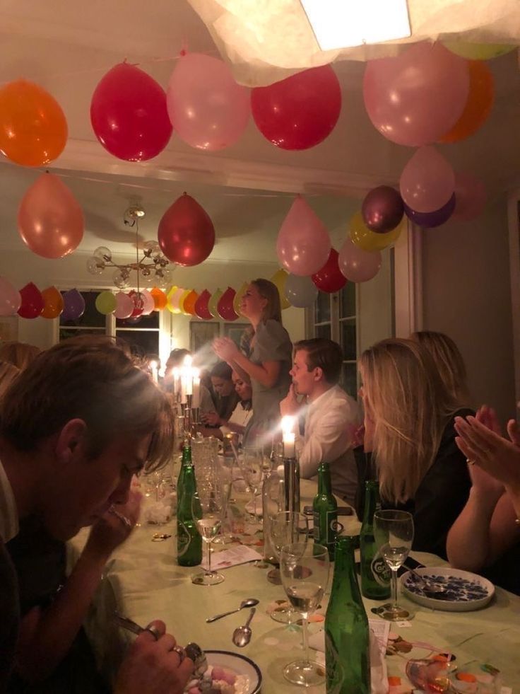 a group of people sitting around a table with plates and wine glasses on it, surrounded by balloons