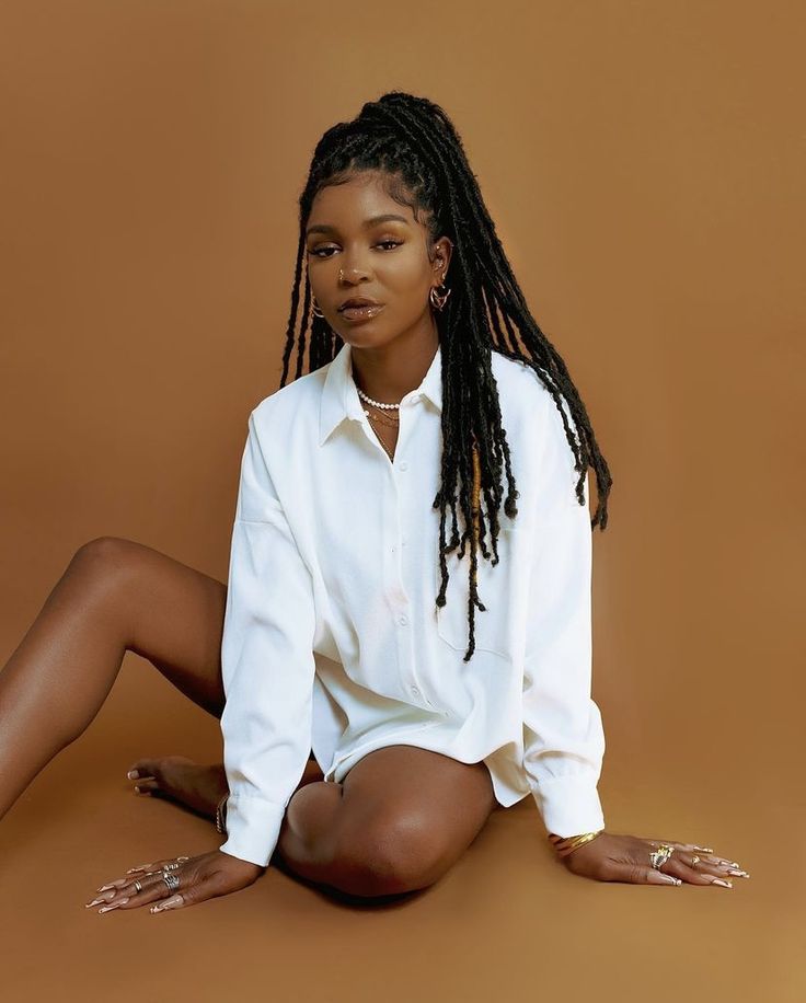 a woman with dreadlocks sitting on the ground in front of a brown background