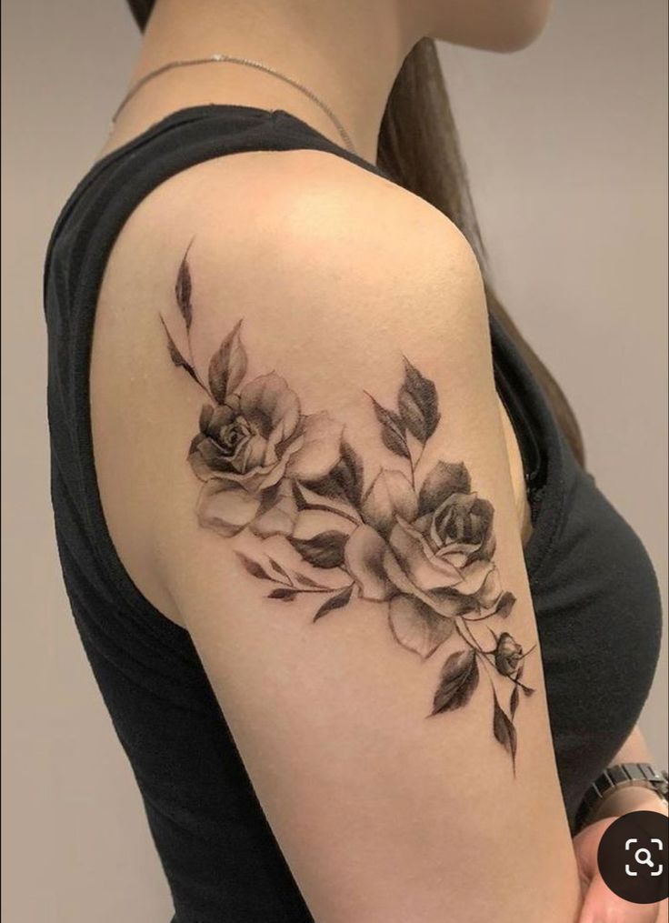 a woman's shoulder with roses and leaves tattooed on her left arm, in black ink