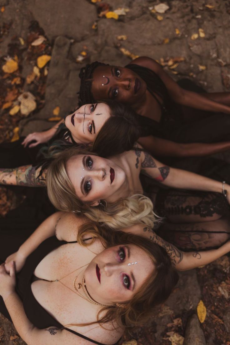 four women with tattoos on their bodies laying in the leaves and looking at the camera