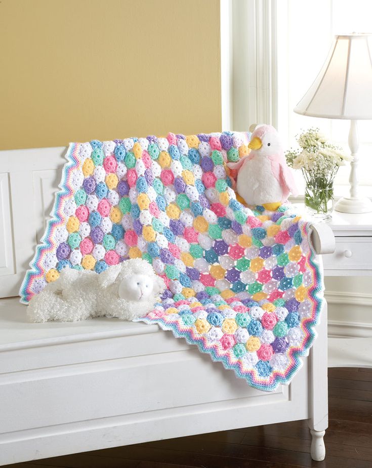 a crocheted blanket is sitting on a bench with two stuffed animals next to it