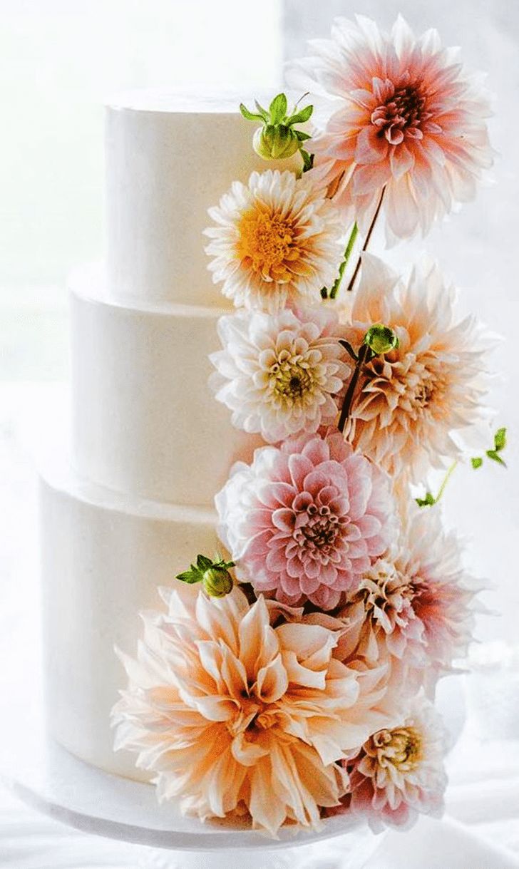 a three tiered white cake with pink and yellow flowers on it's side