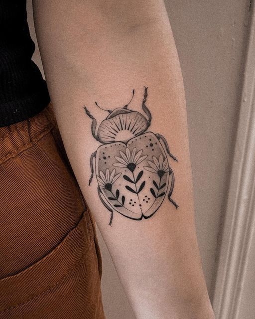 a ladybug tattoo on the arm with flowers and leaves in black ink is shown