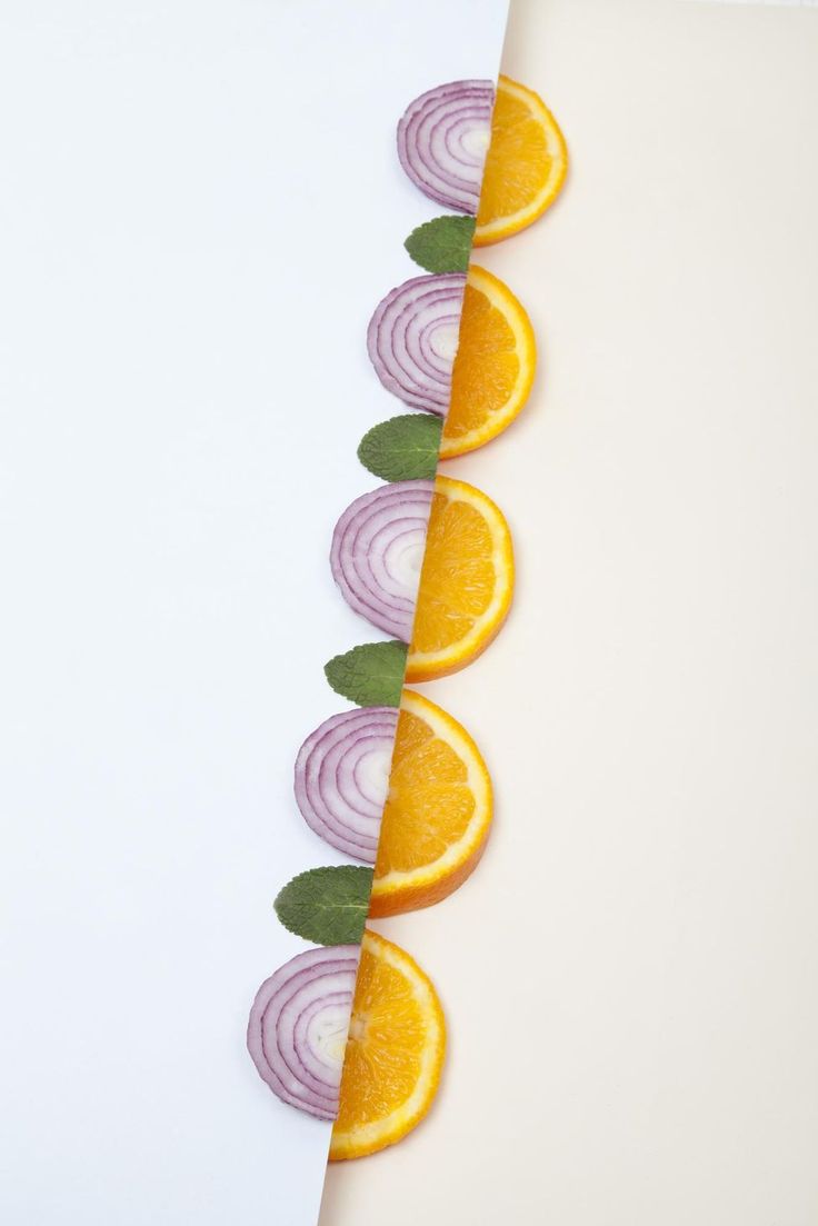 an orange and onion cut in half on top of a white paper with green leaves