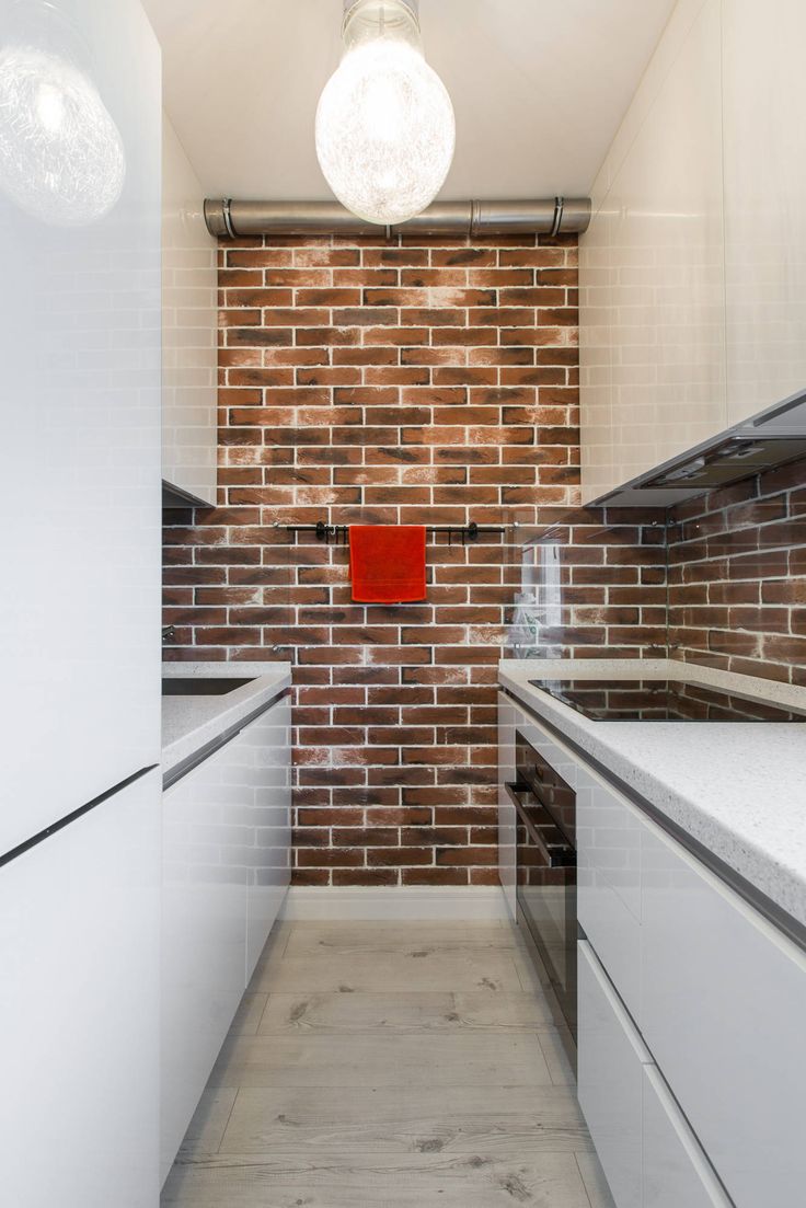 a brick wall in a kitchen with white cabinets and counter tops, along with a red light hanging from the ceiling