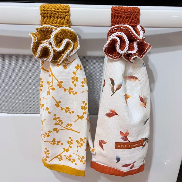 two kitchen towels hanging on the side of a white stove top burner with autumn leaves