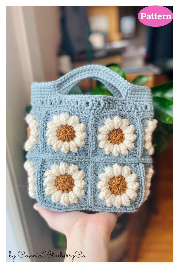 a hand holding a crocheted purse with flowers on it's front and sides