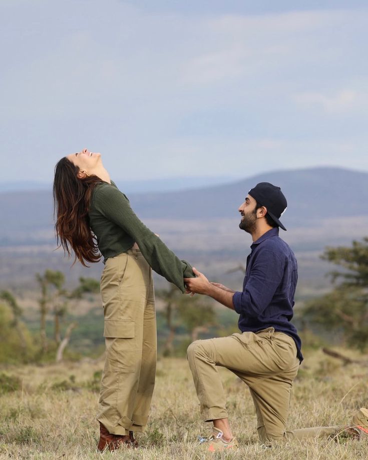 a man kneeling down while holding the hand of a woman's leg in an open field