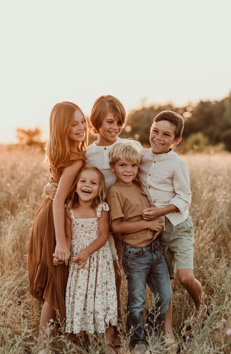 a group of young children standing next to each other in a field with tall grass