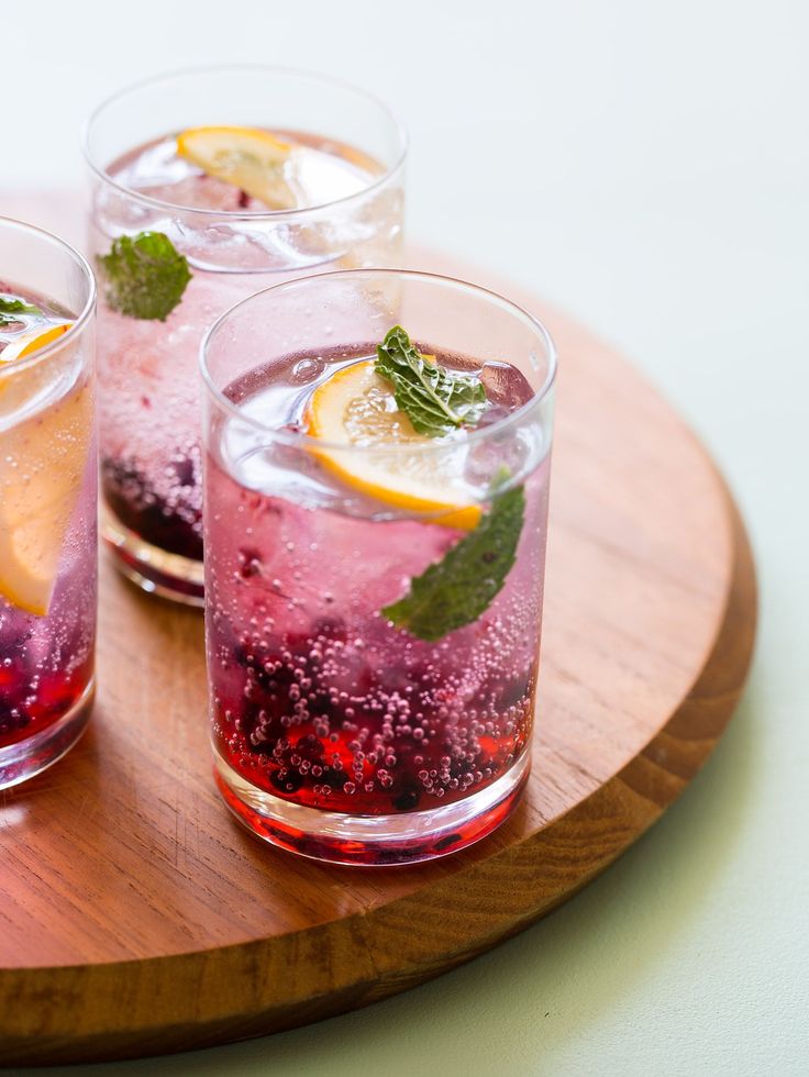 three glasses filled with drinks sitting on top of a wooden tray