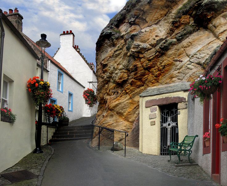 a narrow street with flowers growing on the windows and steps leading up to a rock face