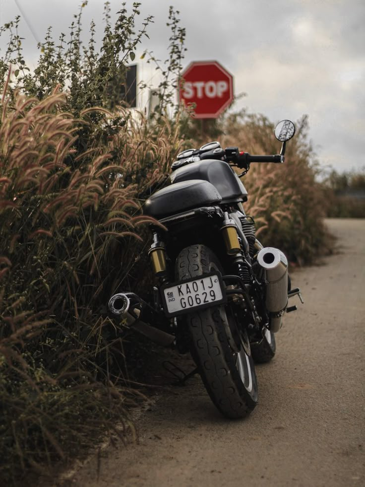 a motorcycle parked on the side of a road next to bushes and a stop sign