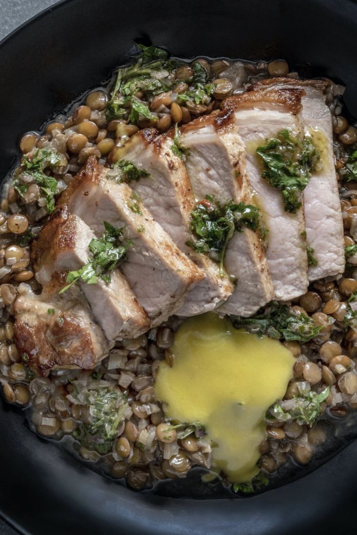 some food is in a black bowl with yellow sauce on the side and garnished with greens