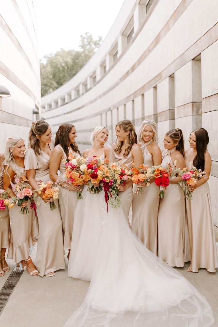 a group of women standing next to each other holding bouquets in front of a building