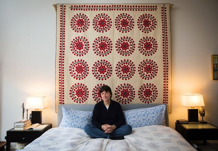 a woman sitting on top of a bed in front of a wall hanging with a quilt