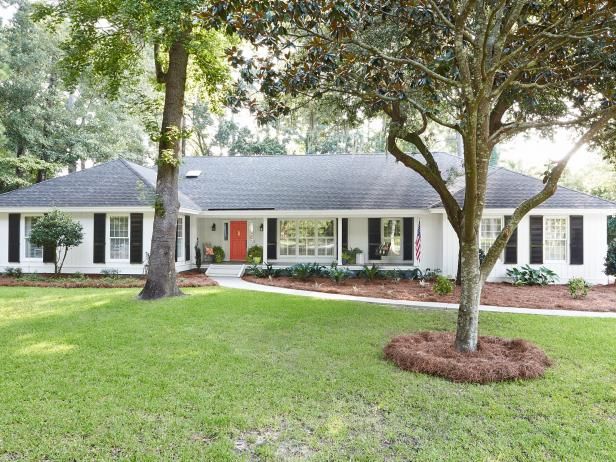 a white house with black shutters on the front and red door is surrounded by trees