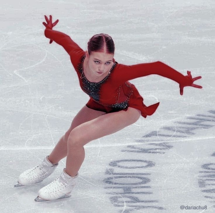 a woman skating on an ice rink wearing a red outfit and holding her arms out in the air