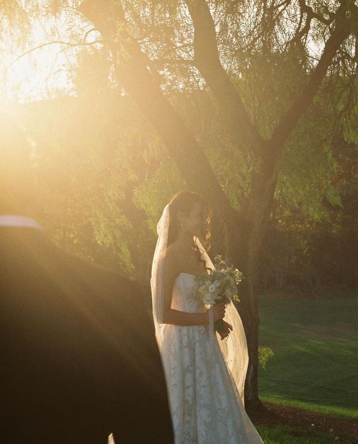 a bride and groom standing in front of a tree at their outdoor wedding ceremony with the sun shining on them