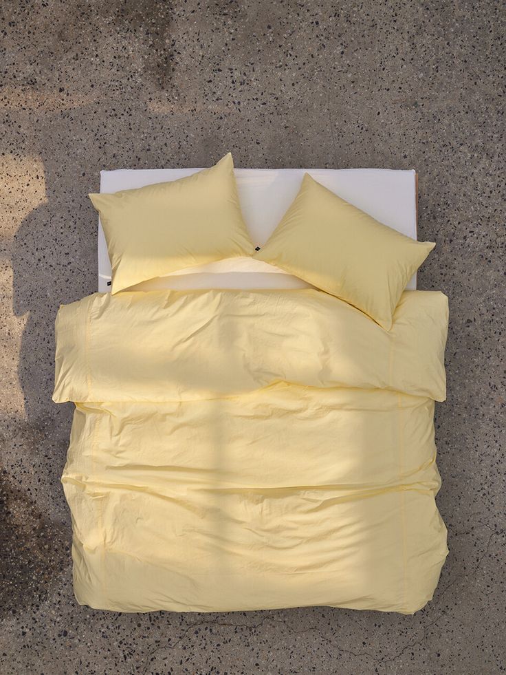 an overhead view of a bed with yellow sheets and pillows on concrete floored area