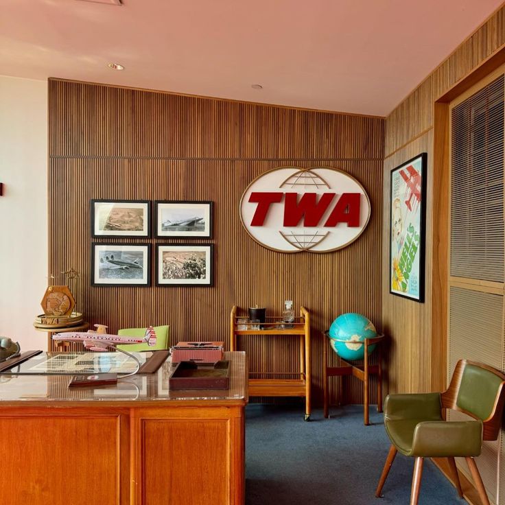 an office with wood paneling and two chairs in front of the desk, there is a twa sign on the wall