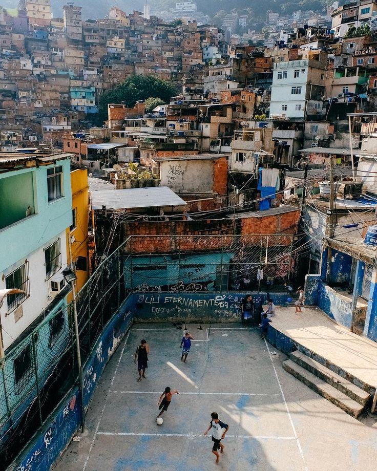 several people playing basketball in an urban area with buildings and hills in the back ground