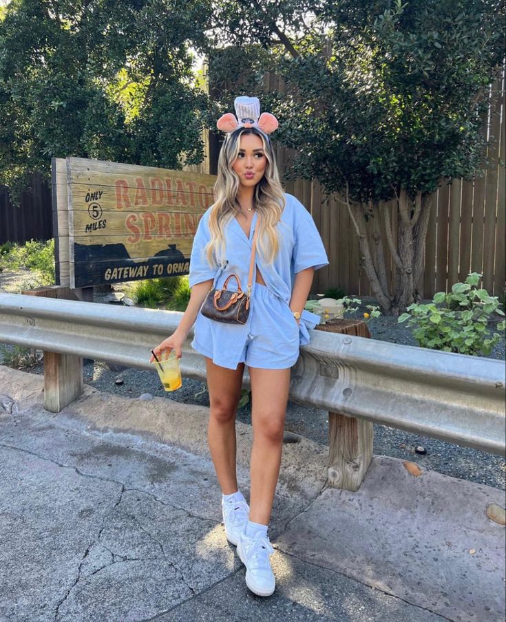 a woman standing in front of a sign wearing a mouse ears hat and blue romper